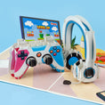 Load image into Gallery viewer, gaming pop up birthday card for gamers - lifestyle image of pop up card open featuring a controller, headset and a computer monitor behind