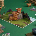 Load image into Gallery viewer, Highland Cow Pop Up Card on a bold green backdrop with props.