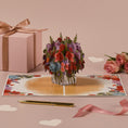 Load image into Gallery viewer, Love Bouquet Pop Up Card by Cardology for Valentines Day Cards or Mothers Day Cards - lifestyle image of the card open with roses and gifts surrounding it