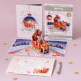 Load image into Gallery viewer, Santa Sleigh Christmas Pop Up Card with Rudolf the rednose reindeer - christmas cards - lifestyle image of card open with notecard and envelope