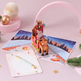 Load image into Gallery viewer, Santa Sleigh Christmas Pop Up Card with Rudolf the rednose reindeer - christmas cards - lifestyle image of the card open with the notecard