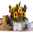 Load image into Gallery viewer, Sunflowers Pop Up Card by Cardology which is perfect for Birthdays, Mothers Day, Anniversaries or even New Home Congratulations. This image is a close up of the pop up which is a beautiful 3D flower arrangement of sunflowers in a vase sitting on a kitchen table top.