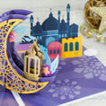 Load image into Gallery viewer, Close up image of the Eid Card on a grey background with gold props