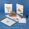 Load image into Gallery viewer, Harry Potter Christmas Pop Up Card - Lifestyle Image with card open, notecard, envelope and packaging in a lifestyle setting with props