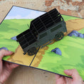 Load image into Gallery viewer, Image showing a pair of hands holding the landrover pop up card open with a map background