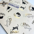 Load image into Gallery viewer, A close-up of a cat-themed gift bag black cat illustrations and gold foiled lettering with words 'MEOW', 'STRETCH', and 'POUNCe' in black and gold foil, and a white paper tag reading 'BATTERSEA HERE FOR EVERY DOG AND CAT'
