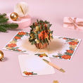 Load image into Gallery viewer, Festive poinsettia basket pop-up card on a table, with a 3D arrangement of red poinsettia flowers and holly as a centrepiece
