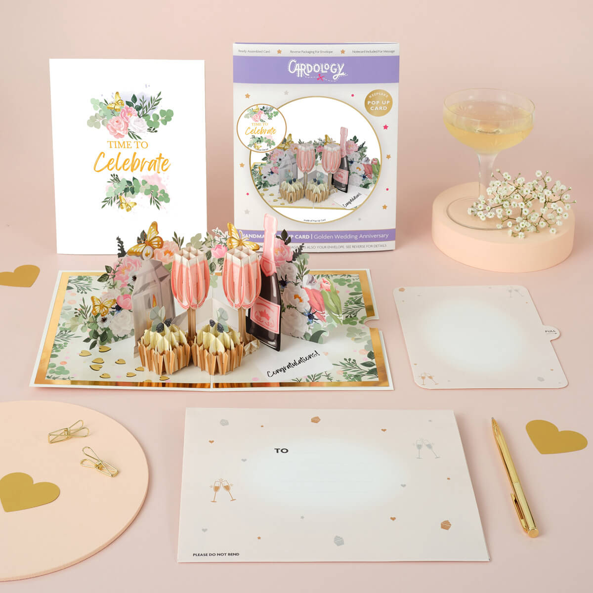 lifestyle image of the celebratory love pop up card which shows all components of the card which includes pop up card, envelope, notecard, card front cover and card packaging - by Cardology