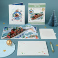 Load image into Gallery viewer, Christmas Train Pop Up Card by Cardology-  lifestyle image showing the 3D train card open, with the notecard, reversible packaging and envelope
