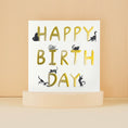 Load image into Gallery viewer, Lifestyle Image of Happy Birthday Cats Card. White with gold foiling with lots of black cats perching on the letters.
