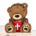 Load image into Gallery viewer, Close up image of Christening Bear Pop Up Card featuring a fluffy brown teddy bear holding a red bible with a cross on the cover
