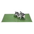 Load image into Gallery viewer, Friesian Cows Pop Up Card featuring 4 3D cows standing next to each other grazing, fully open
